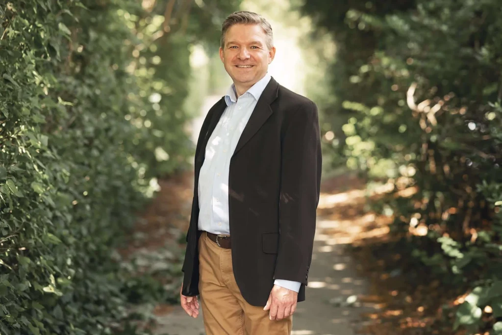 Business portrait of a man in a dark blazer beside green trees Business portrait of a man in a dark blazer beside green trees