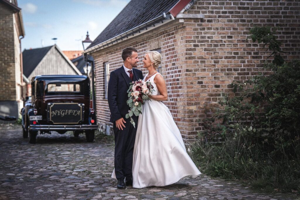 Wedding couple with a bouquet on a cobbled street with a vintage car in the background