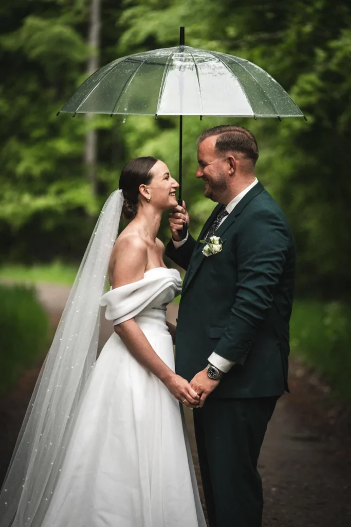 Wedding couple standing close together under a transparent umbrella