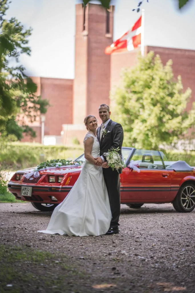 Wedding couple beside a church with a red vintage car in the background