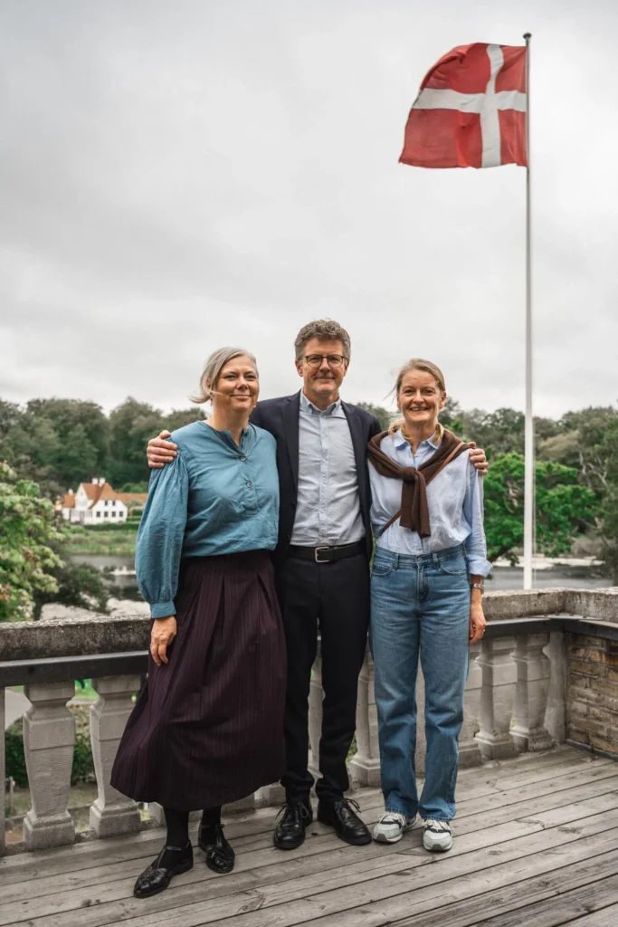 Three celebration guests on a terrace beneath a Danish flag Three celebration guests on a terrace beneath a Danish flag