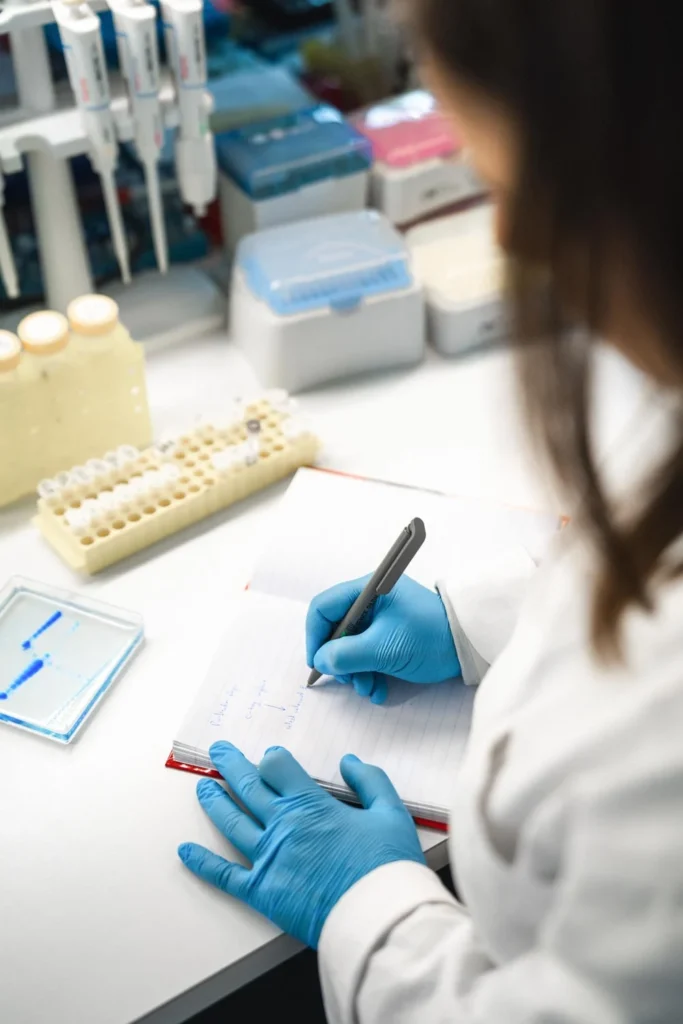 Person wearing blue gloves writing at a workstation Person wearing blue gloves writing at a workstation
