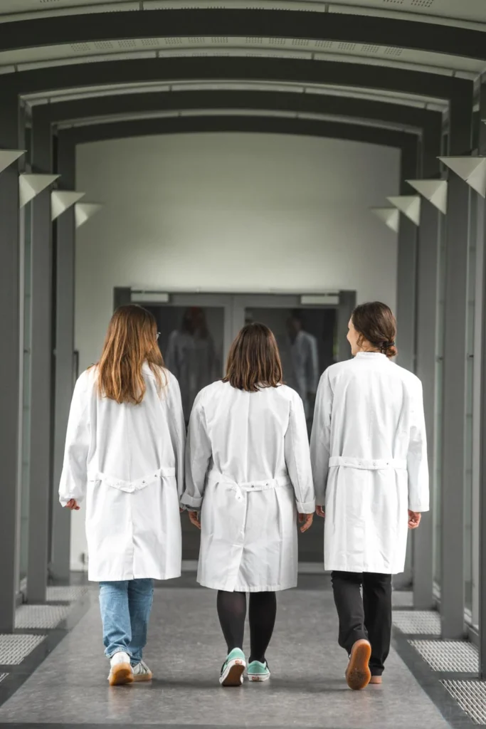 Three people in white coats walking through a laboratory setting